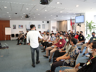 A person standing in front of a group of people in a room

Description automatically generated